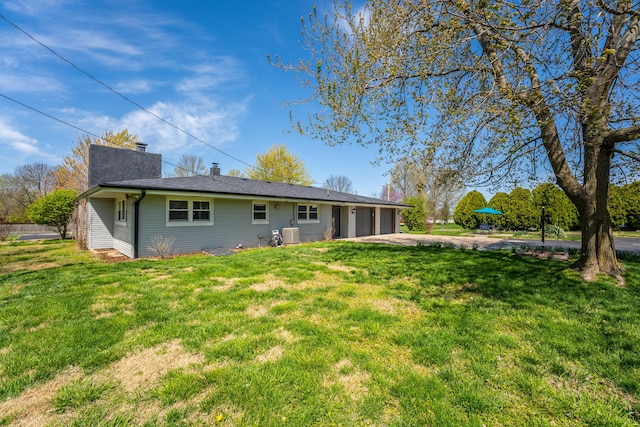rear view of property with a lawn, an attached garage, and driveway