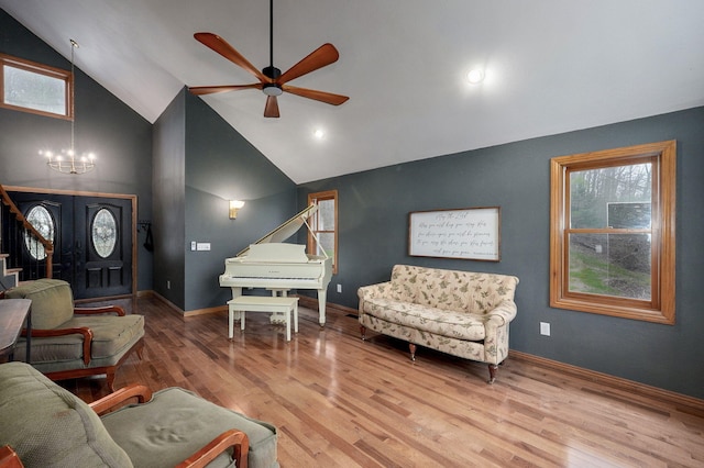 living area featuring plenty of natural light, vaulted ceiling, wood finished floors, and ceiling fan with notable chandelier