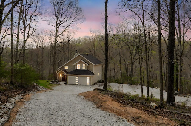 view of front of home featuring an attached garage, driveway, a shingled roof, and a chimney