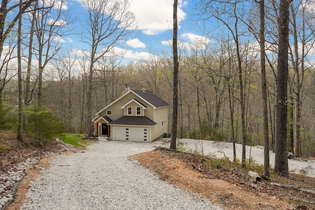 view of front of house featuring a forest view, an attached garage, driveway, and roof with shingles