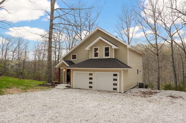 view of front facade with cooling unit, an attached garage, driveway, and roof with shingles