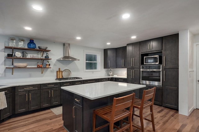 kitchen featuring wall chimney exhaust hood, stainless steel appliances, a kitchen breakfast bar, and light wood-style floors