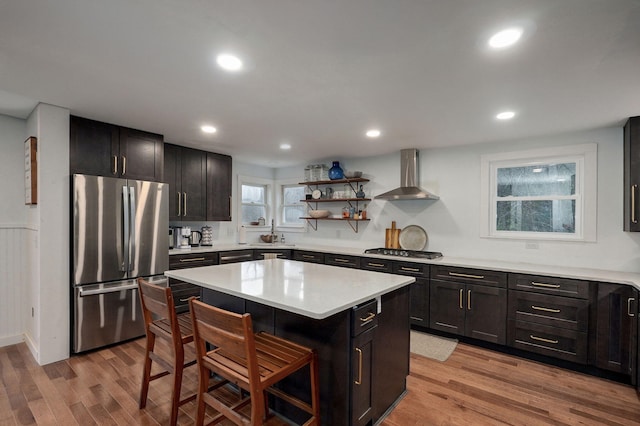 kitchen featuring a breakfast bar, light wood-type flooring, stainless steel appliances, wall chimney exhaust hood, and a kitchen island