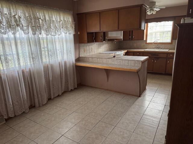 kitchen featuring a peninsula, a sink, tasteful backsplash, ceiling fan, and light tile patterned floors