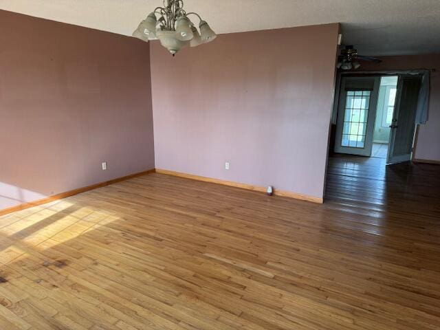 spare room featuring a chandelier, wood finished floors, and baseboards