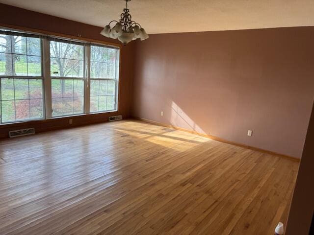 unfurnished room with an inviting chandelier, wood finished floors, visible vents, and baseboards