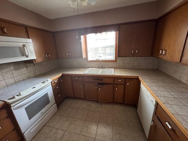 kitchen featuring tile counters, a sink, light tile patterned flooring, white appliances, and decorative backsplash