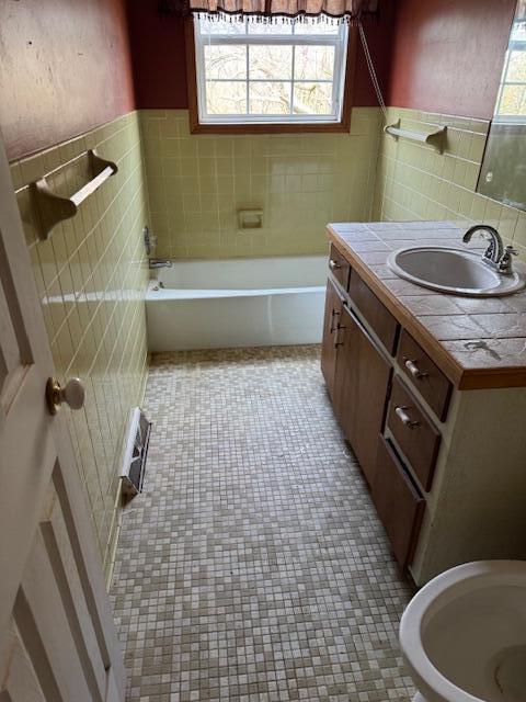 bathroom featuring tile patterned floors, vanity, a bath, tile walls, and wainscoting