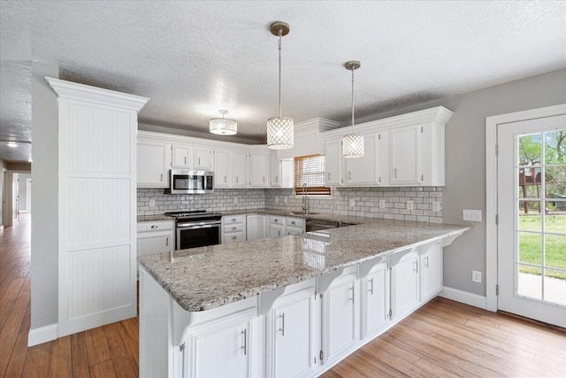 101 Poindexter Dr, Pineville, MO 64856 - kitchen with white cabinets, a peninsula, light wood-type flooring, decorative backsplash, and appliances with stainless steel finishes