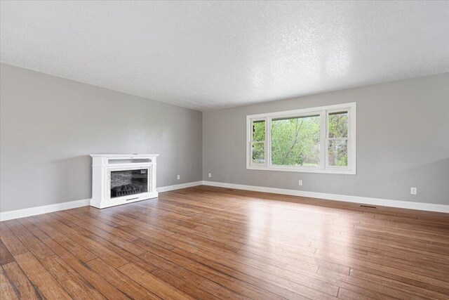 101 Poindexter Dr, Pineville, MO 64856 - unfurnished living room with hardwood / wood-style floors, baseboards, a fireplace, and a textured ceiling