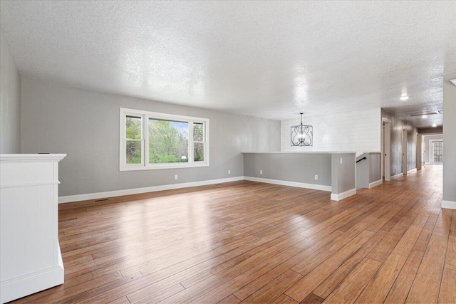 101 Poindexter Dr, Pineville, MO 64856 - unfurnished living room featuring light wood-type flooring, baseboards, an inviting chandelier, and a textured ceiling