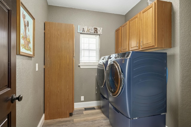 washroom featuring washing machine and dryer, light wood-style floors, a textured wall, and cabinet space