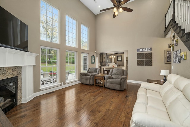 living area featuring a glass covered fireplace, ceiling fan, dark wood finished floors, a high ceiling, and visible vents