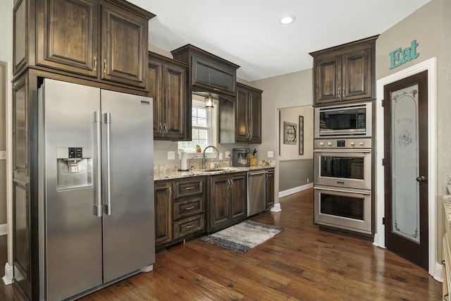 kitchen featuring stainless steel appliances, dark wood finished floors, baseboards, dark brown cabinetry, and light stone counters