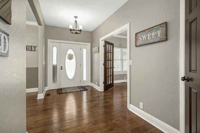 foyer with a chandelier, a textured wall, baseboards, and wood finished floors