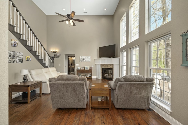 living area featuring dark wood-style flooring, a high ceiling, stairway, ceiling fan, and a fireplace