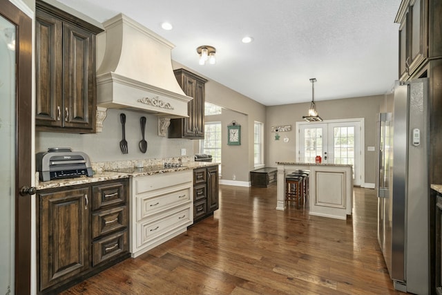 kitchen with dark brown cabinets, black electric cooktop, custom range hood, baseboards, and freestanding refrigerator