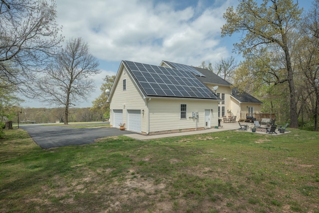 rear view of property featuring a lawn, aphalt driveway, an outdoor fire pit, roof mounted solar panels, and an attached garage