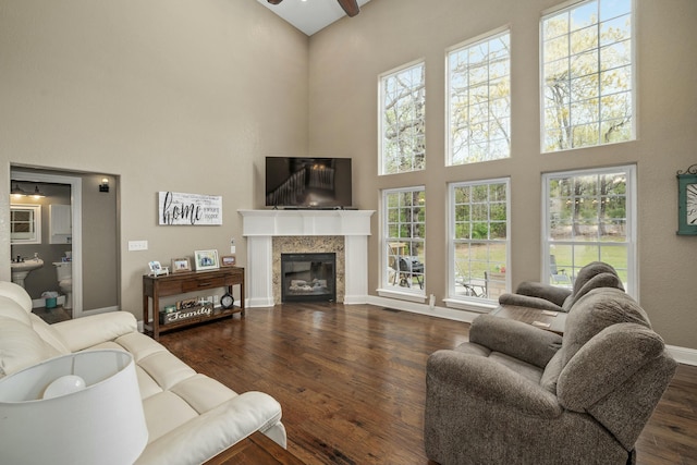 living room featuring ceiling fan, a high ceiling, dark wood-style floors, and baseboards