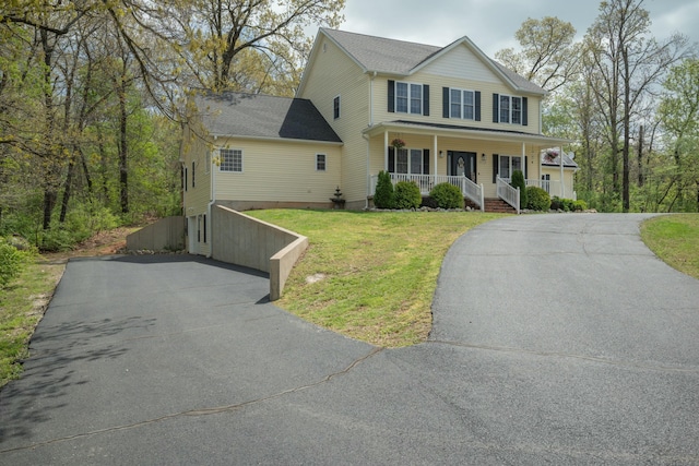 colonial house featuring aphalt driveway, a front yard, and covered porch