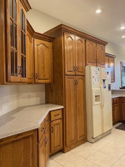 4822 S Montrose Pl, Springfield, MO 65810 - kitchen featuring light tile patterned flooring, recessed lighting, glass insert cabinets, brown cabinetry, and white fridge with ice dispenser