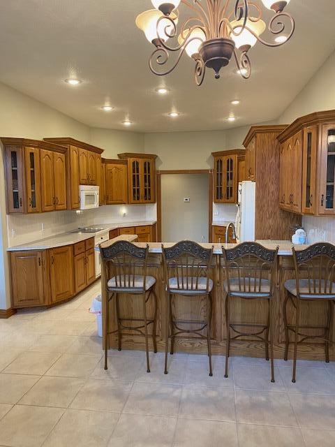4822 S Montrose Pl, Springfield, MO 65810 - kitchen featuring backsplash, white appliances, glass insert cabinets, a chandelier, and brown cabinetry