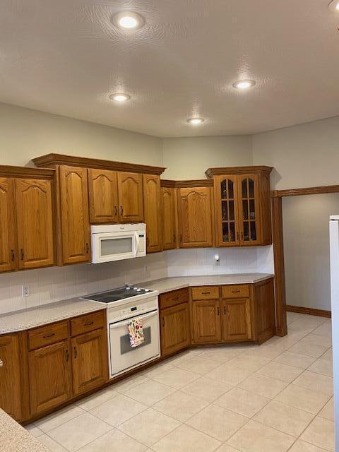 4822 S Montrose Pl, Springfield, MO 65810 - kitchen with light countertops, brown cabinetry, glass insert cabinets, and white appliances