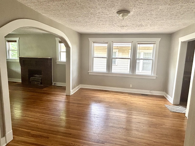 535 E Normal St, Springfield, MO 65807 - unfurnished living room featuring wood finished floors, arched walkways, plenty of natural light, and a textured ceiling