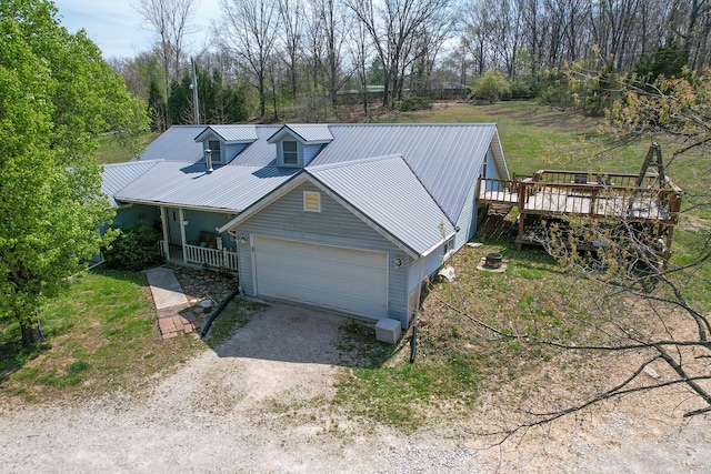 exterior space featuring dirt driveway, metal roof, an attached garage, covered porch, and a deck