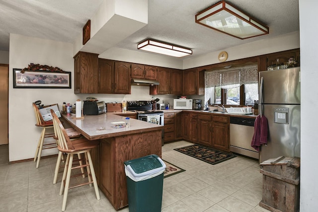 8100 Creek Rd, Hartville, MO 65667 - kitchen with under cabinet range hood, a peninsula, appliances with stainless steel finishes, and light tile patterned floors