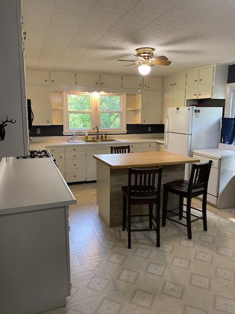 kitchen featuring light countertops, open shelves, ceiling fan, and a sink