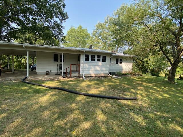 back of property with an attached carport and a yard
