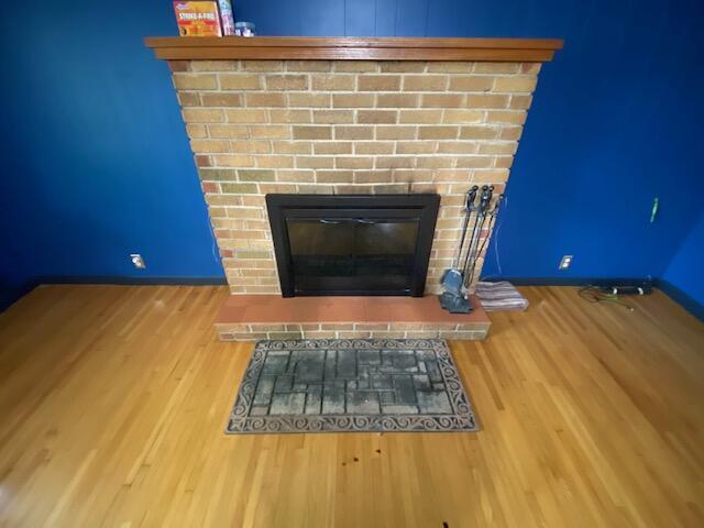 interior details with wood finished floors, a brick fireplace, and baseboards