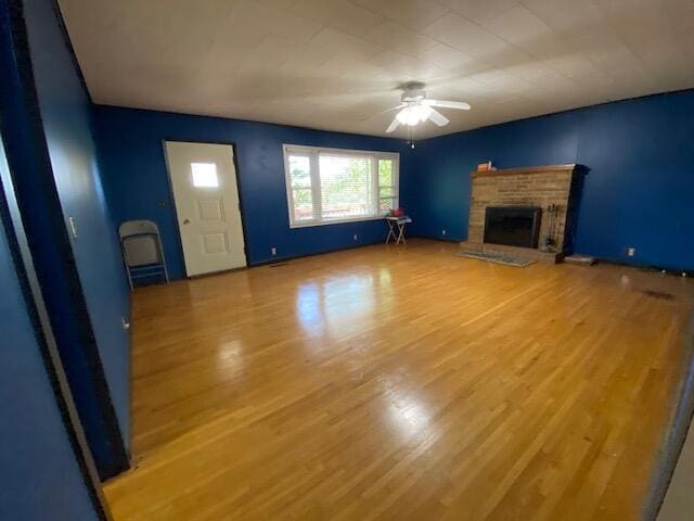 unfurnished living room featuring a ceiling fan, wood finished floors, and a fireplace