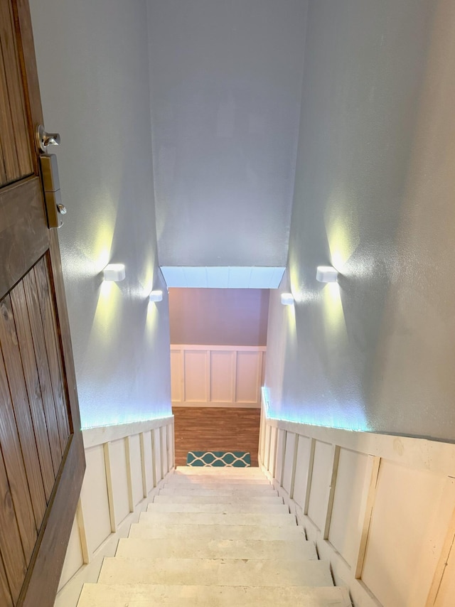 staircase featuring wainscoting, vaulted ceiling, wood finished floors, and a decorative wall