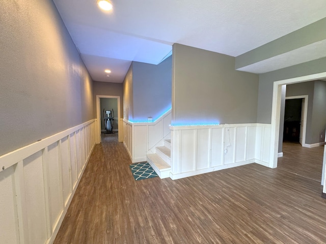 corridor with dark wood-type flooring, a decorative wall, and a wainscoted wall