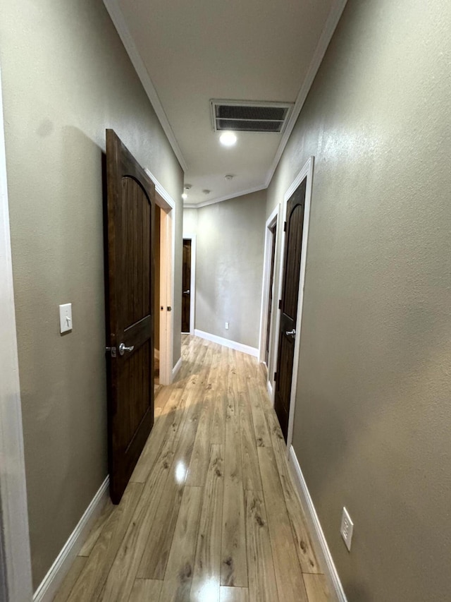 hall featuring baseboards, visible vents, light wood-style floors, and crown molding