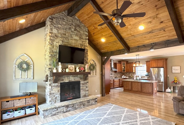 living area featuring light wood-type flooring, beamed ceiling, a ceiling fan, wooden ceiling, and a stone fireplace