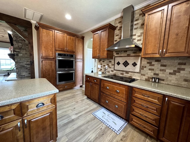 kitchen with arched walkways, black electric cooktop, wall chimney range hood, crown molding, and stainless steel double oven