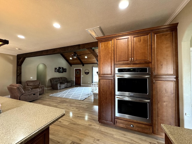 kitchen with light wood-style flooring, open floor plan, vaulted ceiling with beams, stainless steel double oven, and ceiling fan