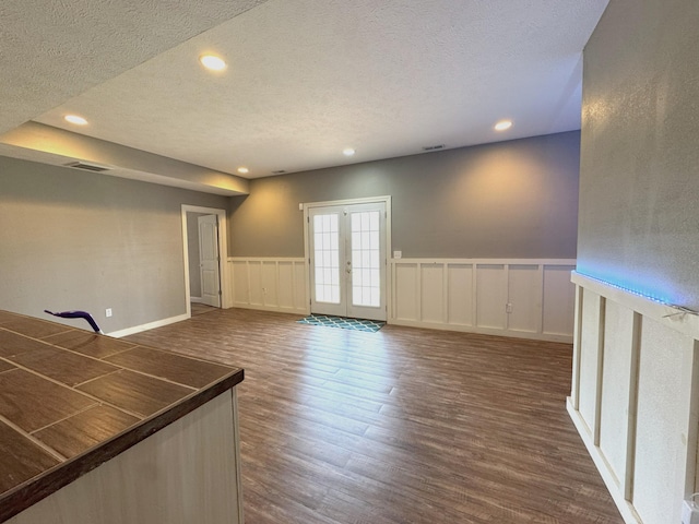 unfurnished room featuring french doors, a textured ceiling, dark wood-style flooring, recessed lighting, and a decorative wall