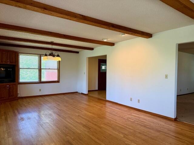 700 Ridgeway, Mountain View, MO 65548 - unfurnished living room featuring an inviting chandelier, baseboards, beam ceiling, and light wood-style floors