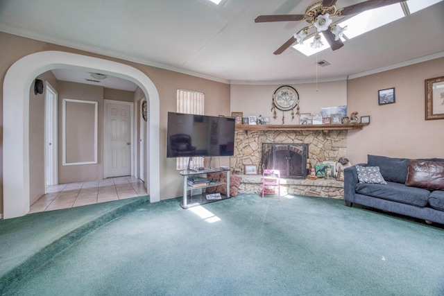 tiled living room featuring a ceiling fan, a stone fireplace, arched walkways, carpet flooring, and visible vents