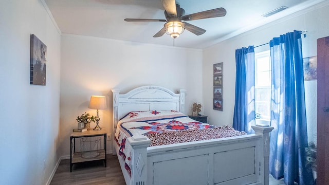 bedroom featuring baseboards, visible vents, wood finished floors, ceiling fan, and ornamental molding