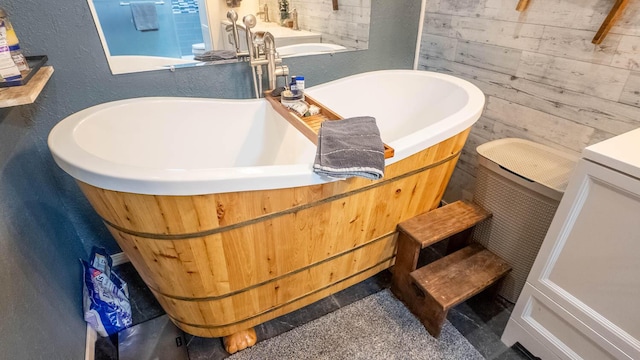 full bathroom with a textured wall, wooden walls, and a freestanding bath