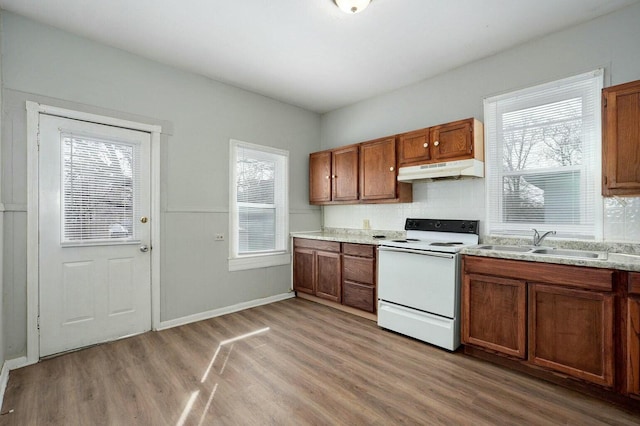 kitchen featuring white electric range oven, a sink, light wood-type flooring, brown cabinets, and under cabinet range hood