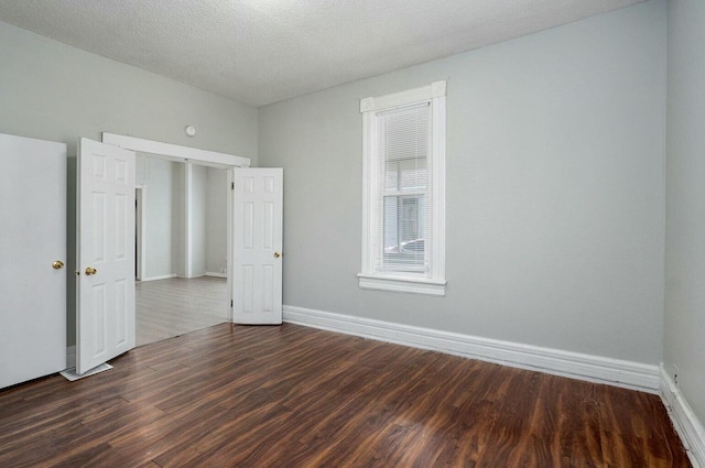 empty room featuring dark wood-type flooring, a textured ceiling, and baseboards