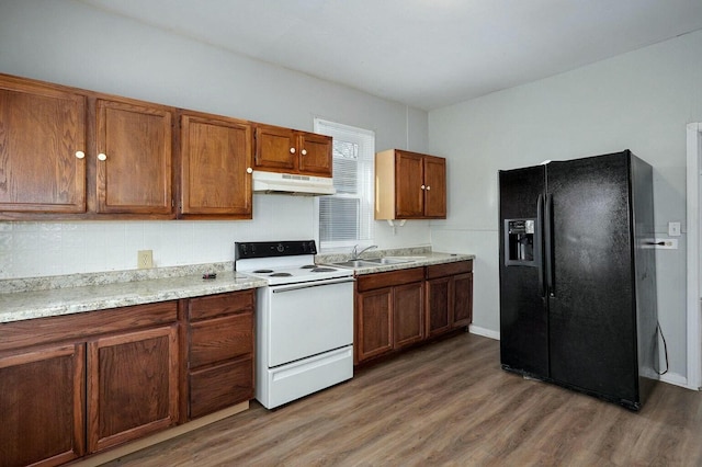 kitchen with wood finished floors, a sink, white electric range, under cabinet range hood, and black fridge