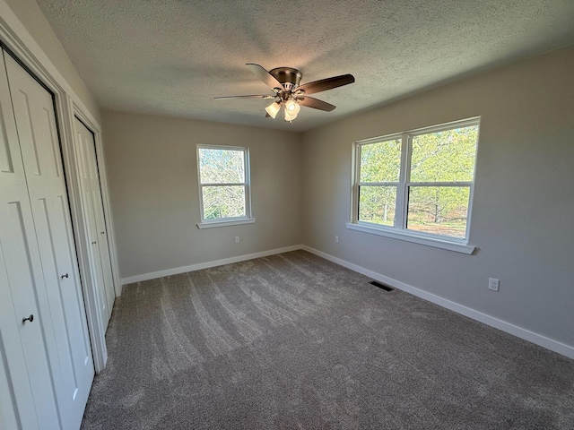 unfurnished bedroom featuring a ceiling fan, a textured ceiling, carpet, baseboards, and visible vents