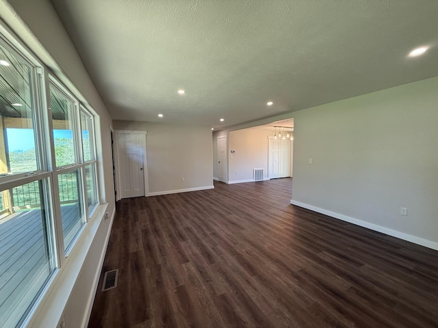 spare room featuring an inviting chandelier, dark wood-type flooring, visible vents, and baseboards